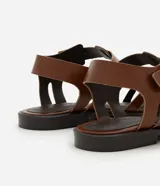 Sandalias planas de cuero marrón con tiras entretejidas, hebilla dorada y suela negra.