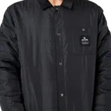 Campera tipo sobrecamisa acolchada de Rip Curl, color negro, con cierre frontal de botones a presión, cuello camisero de pana y bolsillo en el pecho con etiqueta de la marca.