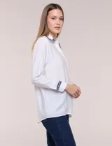 Camisa de crepe liviana y texturada color blanco, de silueta relajada y holgada, con cuello camisero clásico y puños con detalles de bordado de pasamanería con terminación deshilachada y aplique de perlas. Cuenta con cartera de botones oculta al frente y mangas largas.