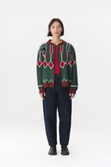 Campera tipo bomber tejida con diseño jacquard geométrico en tonos azul marino, blanco, rojo y verde. Presenta cierre frontal completo, cuello, puños y ruedo acanalados en color verde y blanco, con corte oversized y hombros caídos.