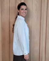 Camisa blanca de algodón con cuello alto tipo mao y volados sutiles a lo largo de la botonadura frontal. Presenta mangas largas con frunces en los hombros y botones frontales.