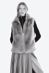 Chaleco de piel sintética con textura suave y efecto peludo, cuello elevado, cierre frontal con cremallera y bajo con elástico oculto para un ajuste abullonado.