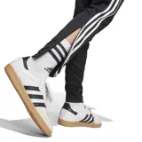 Pantalón deportivo Adidas Tiro 25 Essentials de corte ajustado, color negro con las icónicas tres tiras blancas laterales. Cuenta con pretina elástica con cordón de ajuste, bolsillos laterales con cierre y tecnología AEROREADY para mayor transpirabilidad.