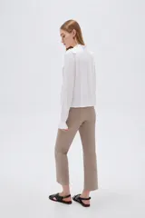 Blusa blanca de viscosa con cuello a la base, mangas largas abullonadas con puños ajustados, detalles de volados, encaje y botones frontales.