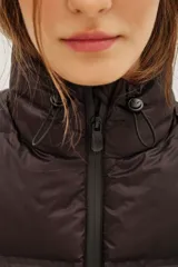 Chaleco acolchado de corte corto, color verde oliva, con cuello alto ajustable mediante cordones elásticos y cierre frontal con cremallera.