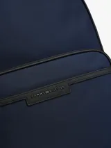 Mochila de poliéster color azul marino con ribetes negros. Presenta un diseño liso, asa superior, correas ajustables y acolchadas, y un panel trasero de malla acolchado. Cuenta con un compartimento principal amplio, funda para portátil incorporada, bolsillo interior con cremallera y bolsillo exterior con cremallera, donde se ubica el logo metálico de Tommy Hilfiger.