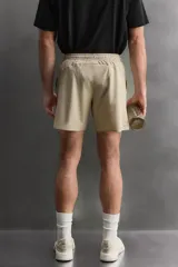 Short deportivo de entrenamiento en color marrón, confeccionado en tejido técnico ligero y elástico. Cuenta con cintura elástica ajustable con cordón, bolsillos frontales, bolsillo trasero con cierre y aberturas laterales en el bajo. Incluye un pequeño detalle de logo estampado en la pierna.