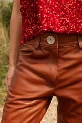 Pantalón de cuero color marrón con estampado abstracto, corte acampanado y abertura en el ruedo.