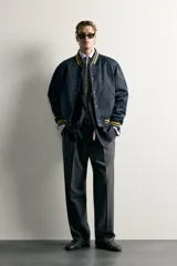 Cazadora bomber estilo universitario, de corte relaxed fit y tejido técnico azul marino, con cuello, puños y dobladillo de rib elástico a rayas amarillas. Cuenta con bolsillos delanteros de plastrón y cierre frontal con botones a presión.