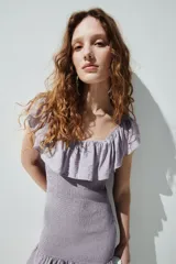 Vestido corto lila de tejido fruncido, con diseño ajustado, hombros descubiertos, escote cuadrado elástico y volados anchos en el escote y en el ruedo.