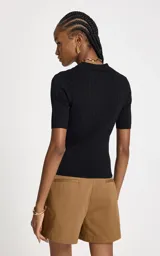 Remera de punto acanalado color negro, con silueta ajustada, cuello polo estructurado, mangas cortas y cierre frontal con cremallera metálica y colgante decorativo.