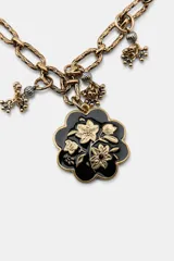 Pack de dos collares de eslabones metálicos labrados en tono dorado envejecido. El collar más largo presenta un dije colgante principal con forma de flor negra y detalles dorados, además de pequeños dijes colgantes. El collar más corto tiene múltiples dijes colgantes que incluyen un corazón amarillo, una piedra rosada, un dije ovalado negro con flores doradas, un dije redondo con flor roja, un dije cuadrado con mariposa negra, y otros dijes pequeños como una perla y un dije negro ovalado.