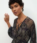 Bata de tul con estampado paisley, de corte holgado y fluido. Presenta escote en V con lazo ajustable, mangas largas amplias y elástico en la cintura que genera un efecto peplum.