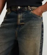 Pantalón de jean con corte baggy, de tiro alto y pierna ancha. Presenta un diseño de estilo vintage con acabado desgastado y trabillas en la cintura.