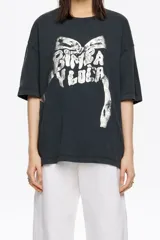 Camiseta larga de corte oversize, color gris oscuro con efecto gastado, confeccionada en algodón. Presenta escote redondo y un estampado frontal en blanco que simula un lazo y el texto "BIMBA Y LOLA".