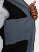 Campera OG Active de Carhartt WIP, color azul grisáceo, con capucha integrada, cierre frontal con cremallera metálica, bolsillos tipo canguro y parche con el logo de la marca en el bolsillo inferior.