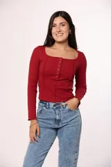 Remera de manga larga en color rojo, confeccionada en tejido acanalado. Presenta un escote cuadrado y una hilera de botones decorativos en el centro del pecho, con costuras expuestas que recorren el frente de la prenda.