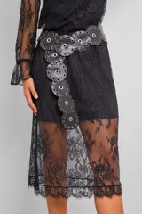 Conjunto de dos piezas compuesto por blusa de encaje semitransparente con cuello alto y mangas largas, y falda midi a juego. Ambas prendas incluyen visos interiores a tono. El diseño presenta un encaje floral delicado en color negro.