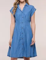 Vestido camisero corto de lyocell en tono azul denim, con cuello camisero, escote en V y cierre frontal con botones. Presenta mangas cortas, cintura entallada con pinzas verticales y falda evasé con vuelo.
