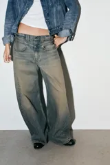 Jeans de tiro bajo con corte baggy y silueta barrel. Presenta diseño de cinco bolsillos, trabillas para cinturón y cierre frontal con cremallera y botón metálico. Confeccionado en denim con efecto de lavado desgastado.