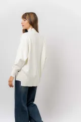 Sweater de tejido de punto color beige, con cuello alto, hombros caídos, mangas largas con puños acanalados y tajos laterales en el ruedo.