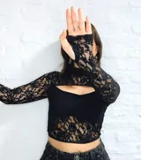 Top tipo corset de encaje negro con mangas largas y abertura en el pecho.