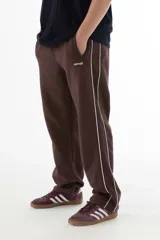 Pantalón de jogging marrón con corte recto, cintura elástica y cordón ajustable. Cuenta con bolsillos laterales y una línea vertical blanca a lo largo de la pierna.