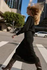 Vestido midi de punto en color negro, con cuello barco y mangas largas con sisa ancha. Presenta una cintura entallada con un cinturón fino incorporado con hebilla metálica dorada.