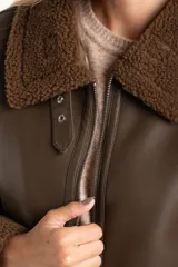 Campera tipo gamulán de cuero sintético marrón con interior y detalles de corderito en cuello, puños y ruedo. Presenta cierre frontal metálico y corte oversize.