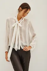 Camisa de transparencia con diseño a rayas verticales, cuello con lazo integrado y mangas largas abullonadas con puños ajustados.