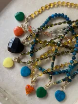 Collar con dije de corazón facetado en color verde esmeralda, con cadena de cuentas de cristal facetadas en tonos amarillos y dorados.