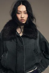 Chaqueta tipo bomber de denim lavado azul, corte holgado, con cuello solapa y aplicación de pelo sintético marrón desmontable. Presenta bolsillos delanteros y bajo acabado en elástico.