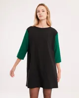 Vestido corto negro con mangas 3/4 verdes, cuello bote y bolsillos laterales.