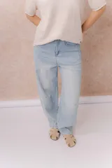 Jean de calce relajado y pierna amplia color beige, con tiro alto y detalle de recortes y costuras visibles.