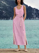 Vestido largo sin mangas color rosado, con escote redondo, bolsillos laterales y detalles de pasamanería en zigzag beige en el cinturón y los tajos laterales.
