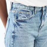 Pantalón jean de corte globo con tiro alto, confeccionado en denim de lavado claro con costuras frontales verticales en el bajo.