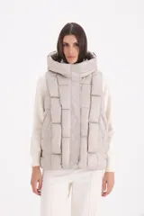 Chaleco acolchado color beige con diseño de cuadros, capucha amplia y cierre frontal oculto.