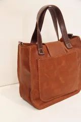 Cartera marrón de cuero con doble asa corta y cierre con solapa y broche metálico.