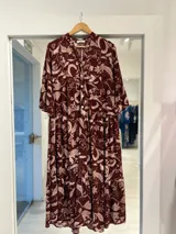 Vestido largo bordó con estampado botánico en tonos claros, escote en V con botones frontales, mangas largas con volados en los puños y diseño de faldas escalonadas.