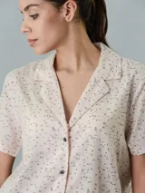 Camisa de pijama de manga corta color beige con estampado de letras negras, cuello clásico y cierre frontal con botones.
