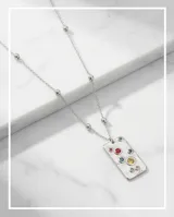 Collar de acero con cadena de eslabones y pequeñas esferas metálicas intercaladas. Presenta un dije rectangular de superficie texturizada con incrustaciones de circonias multicolor.