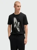 Camiseta negra de manga corta y cuello redondo, con un gráfico abstracto en blanco y negro con textura desgastada en el centro del pecho, y el logo 'BOSS' en la parte inferior izquierda del gráfico.