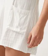 Enterito corto de tirantes finos ajustables, color blanco con rayas verticales finas, escote en V y bolsillos delanteros.