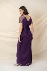 Vestido largo de fiesta color violeta, con cuerpo de jersey y falda de gasa con diseño drapeado y sobrecapa. Presenta escote en V y mangas cortas de tul bordado con pedrería al tono.