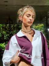 Chomba de piqué con diseño color block vertical en negro y verde oscuro, cuello polo y cierre frontal parcial. Presenta inscripciones en el frente.