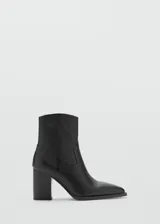 Botín de cuero vacuno color negro, con diseño de estilo western, punta fina y tacón bloque de 6,5 cm. Cuenta con cierre de cremallera lateral.
