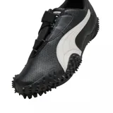 Championes Puma modelo Mostro Perforated, de diseño bajo con exterior de cuero perforado en color blanco y detalles en negro. Presenta una suela distintiva con relieve de tachones y cierre de velcro en el empeine.