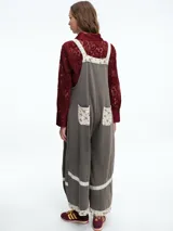 Mono largo de color negro con corte holgado y perneras anchas. Presenta detalles de encaje blanco y tela estampada floral en los tirantes, el bolsillo frontal, la parte inferior de las piernas y el ruedo.