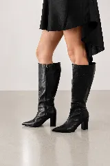 Bota de caña alta confeccionada en cuero genuino color negro, con diseño de punta fina y taco cuadrado de 7.5 cm. Presenta cierre lateral completo para facilitar su colocación.