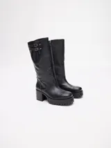 Bota bucanera de cuero vacuno wax color negro, con punta cuadrada, suela de goma con plataforma dentada y taco de madera. Presenta detalle de doble hebilla metálica en la parte superior de la caña.